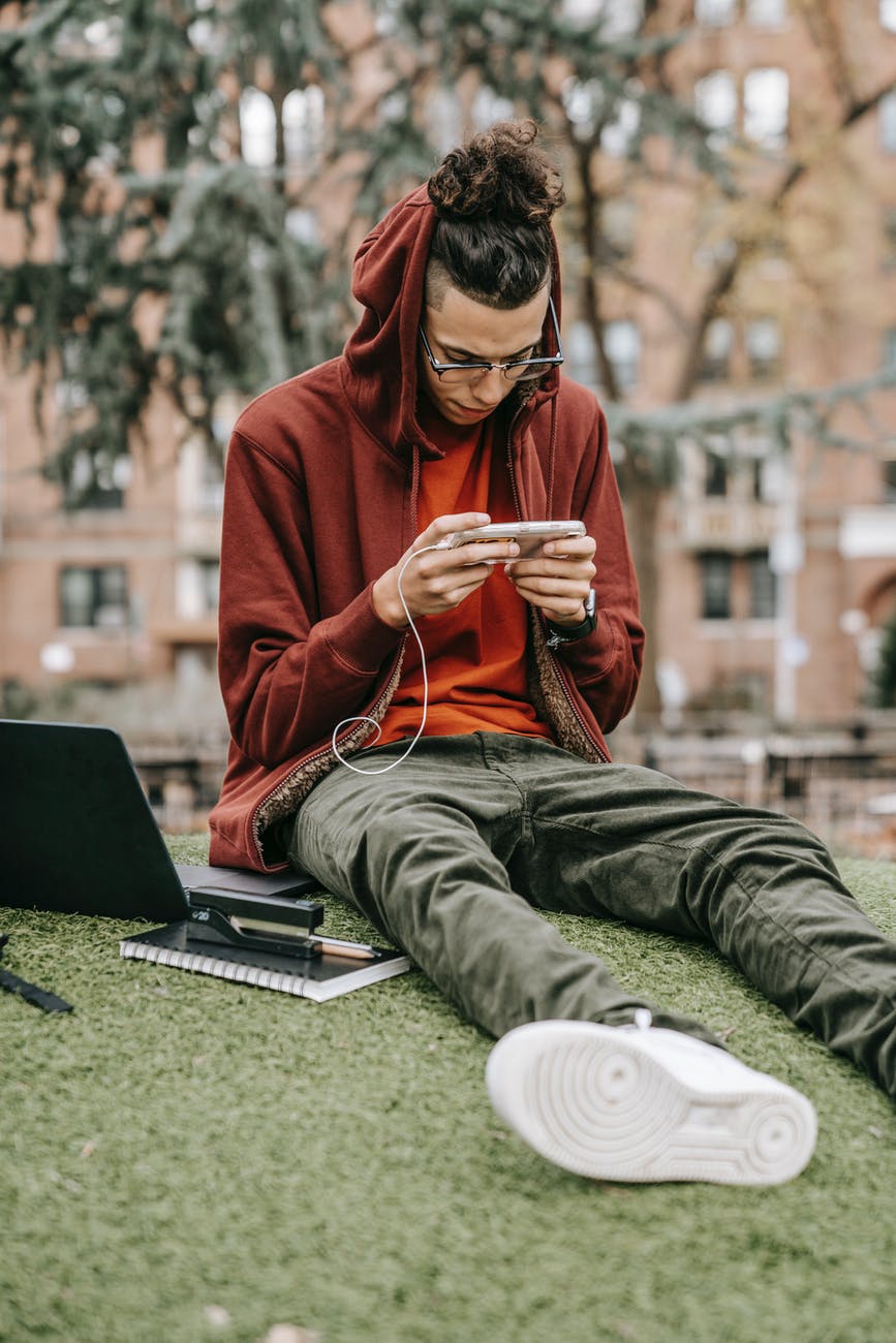 student surfing internet on smartphone on urban lawn