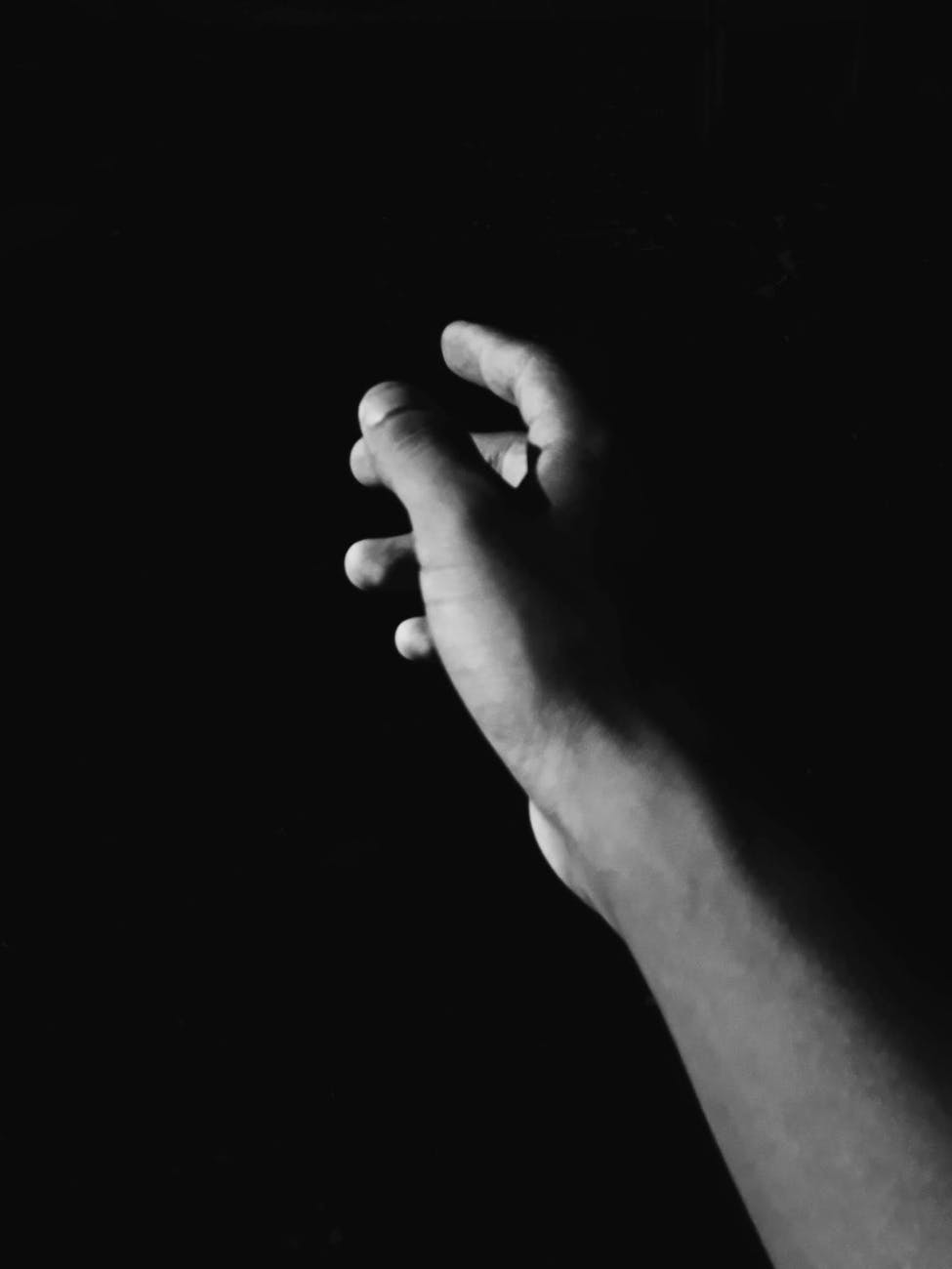 grayscale photo of hand reaching out against black background