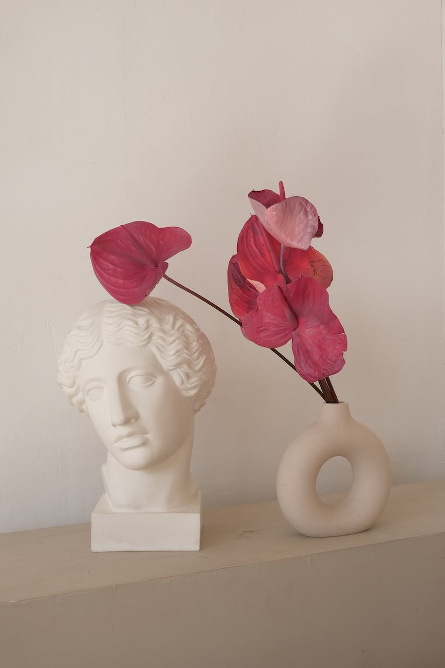 sculpture of male head next to vase of pink anthurium flowers